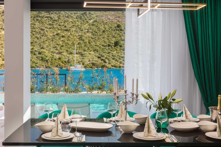 Table à manger dressée avec chaises vertes devant la fenêtre donnant sur la baie