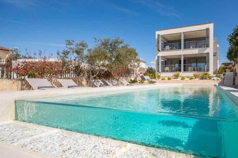 Piscine avec paroi en verre et transats devant l'immeuble neuf moderne