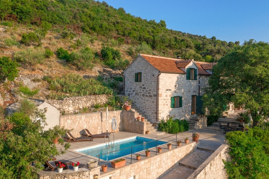 Maison en pierre aux volets verts et piscine devant le mur en pierre sèche