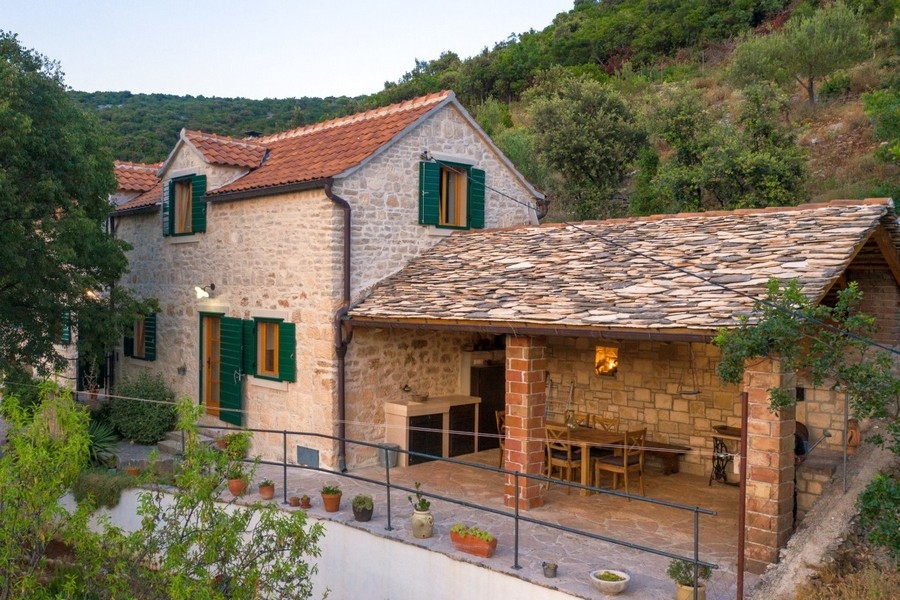 Maison en pierre avec coin repas couvert sous un toit en dalles de pierre