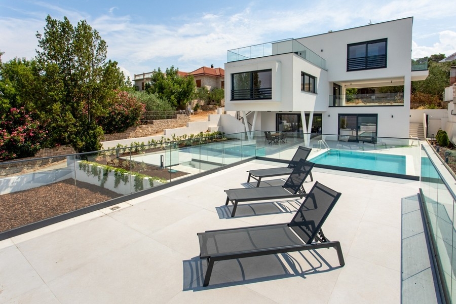 Transats sur la terrasse devant la piscine et la villa blanche