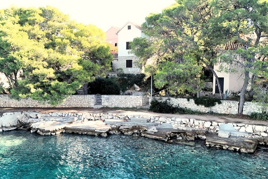 Maison derrière des pins au-dessus de la côte rocheuse avec eau turquoise