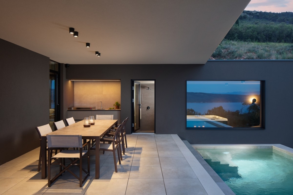 Espace extérieur avec piscine et coin repas couvert dans l'ambiance du soir