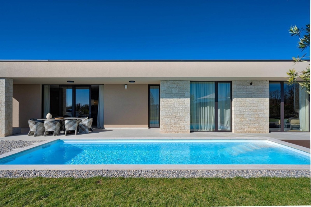 Maison à toit plat avec façade en pierre naturelle et piscine dans la pelouse