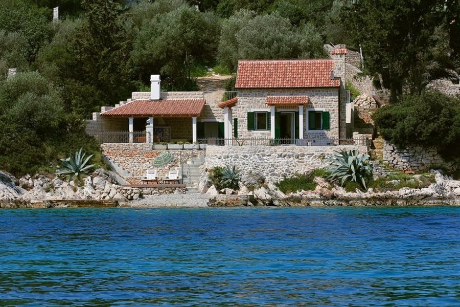 Maison en pierre avec volets verts et agaves sur la rive rocheuse