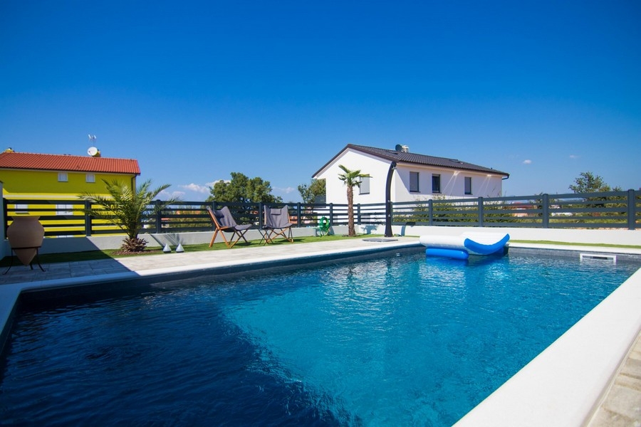 Piscine avec matelas gonflable et palmiers devant la maison blanche