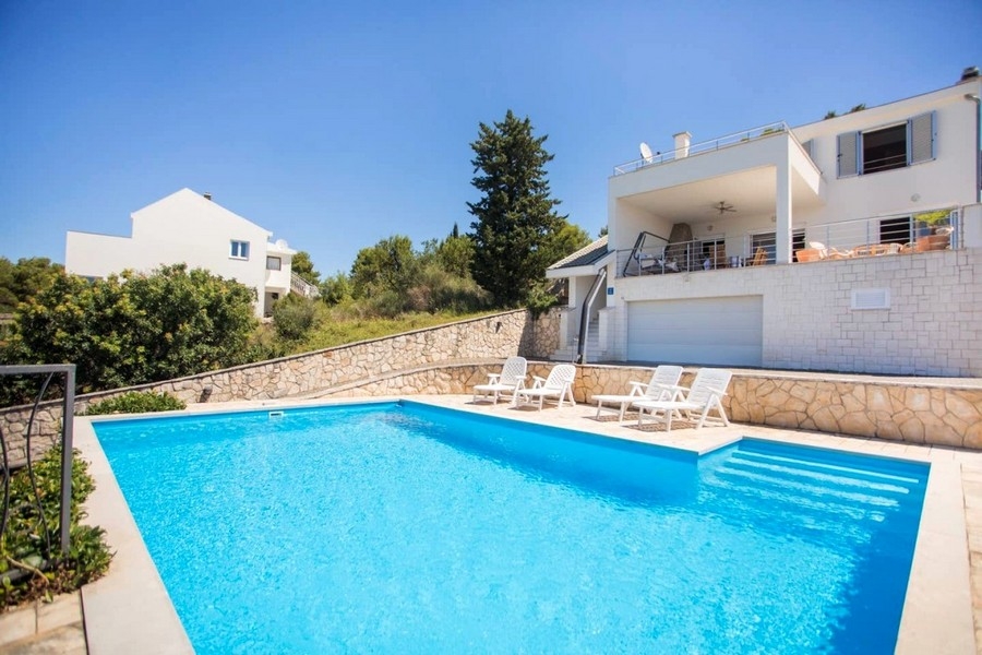 Grande piscine avec bains de soleil devant la villa