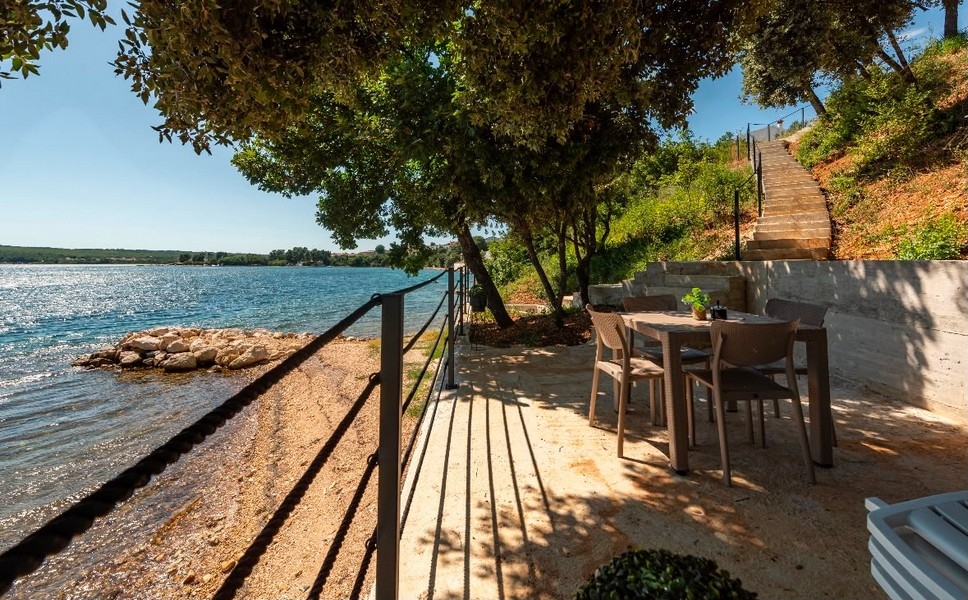 Table à manger au bord de l'eau sous les arbres avec escalier menant à la maison
