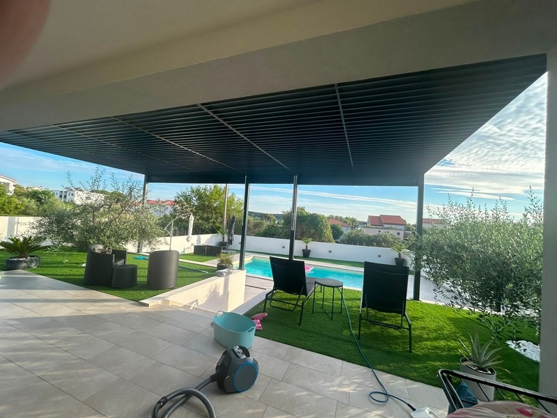 Terrasse couverte avec coin salon, pelouse et piscine