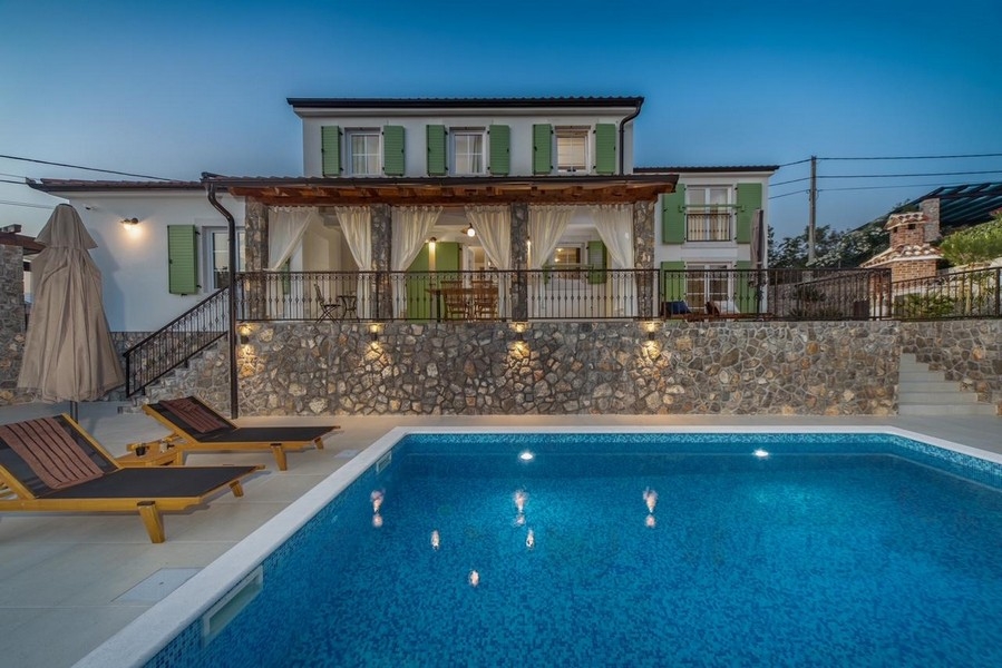 Villa éclairée avec volets verts et piscine le soir