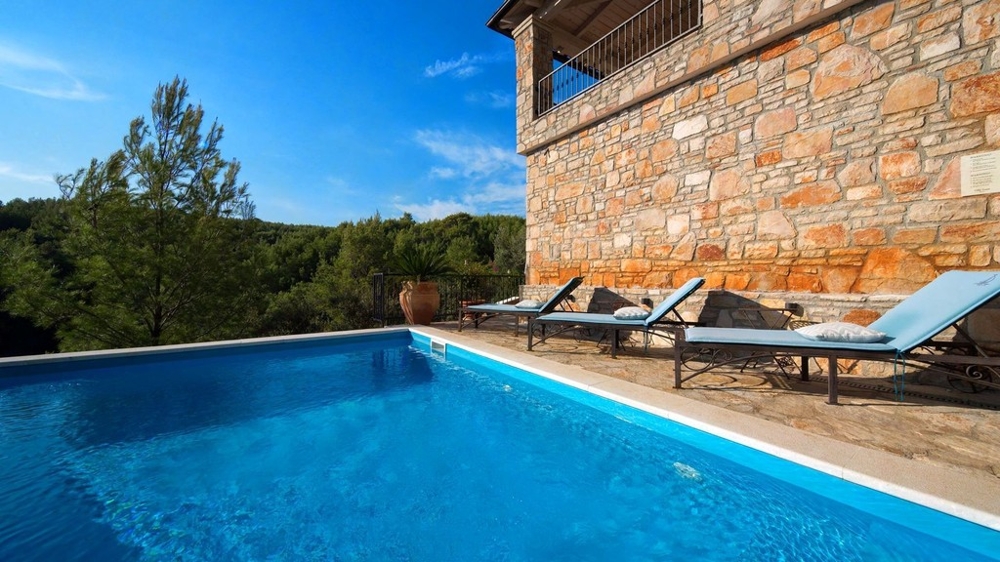 Piscine avec bains de soleil devant la façade en pierre