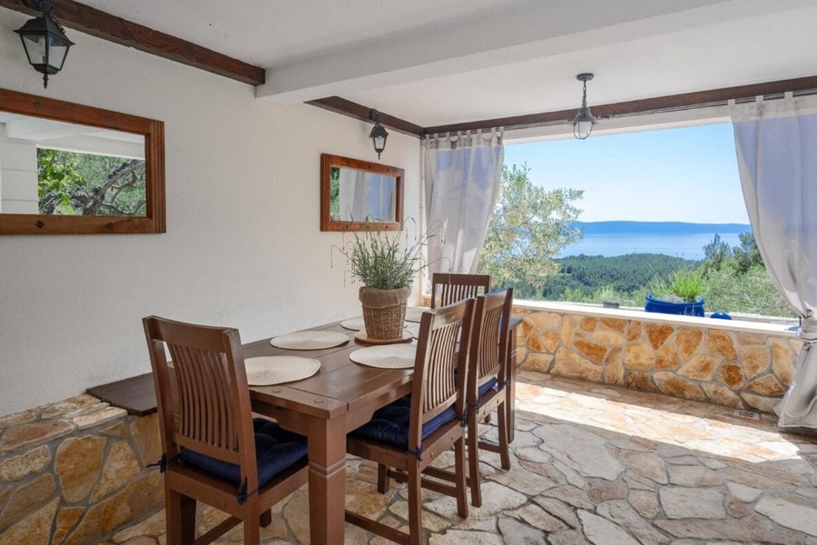 Espace repas couvert avec mur en pierre et vue mer