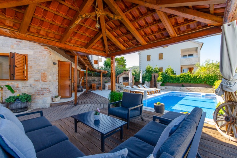Terrasse en bois couverte avec salon de jardin au bord de la piscine