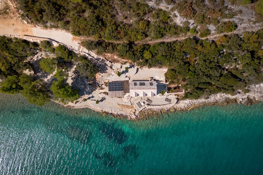 Baie avec maison en pierre, pins et eau turquoise vue d'en haut