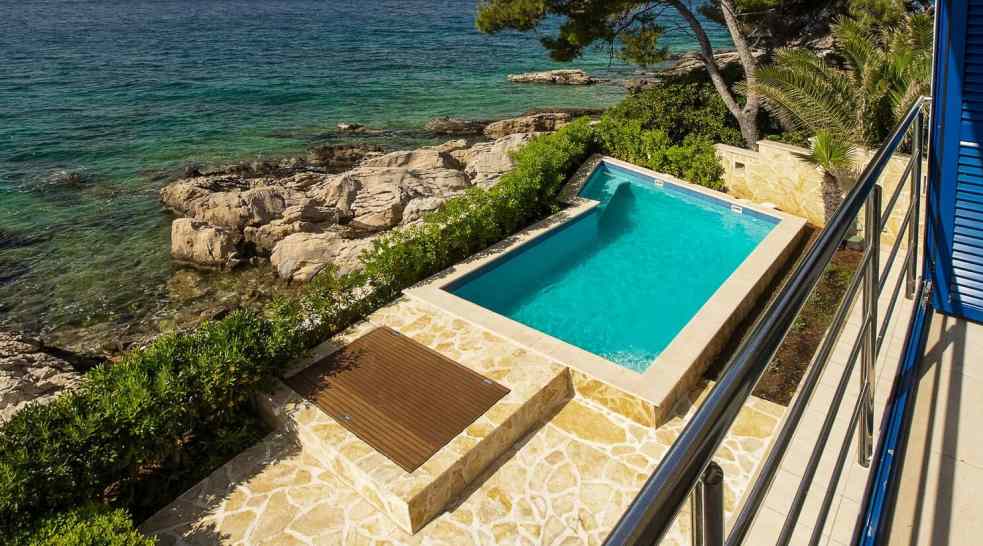 Piscine au-dessus de la côte rocheuse avec terrasse en bois et dalles en pierre naturelle