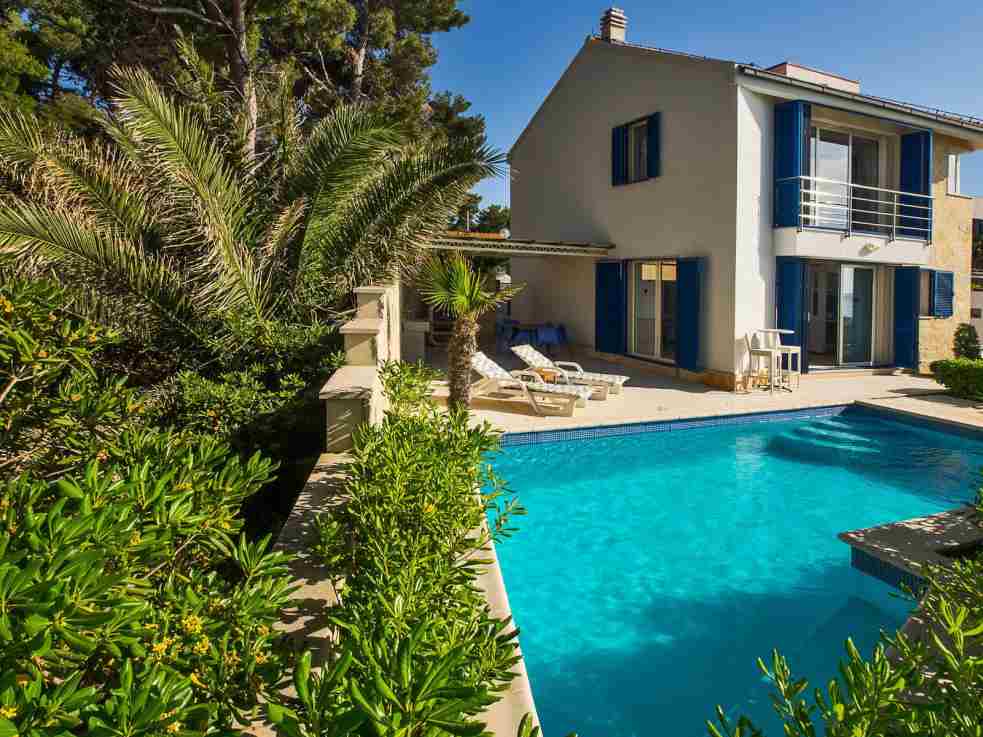 Maison aux volets bleus et piscine derrière des lauriers-roses